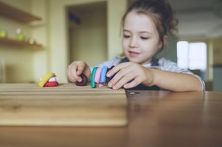 A close up of a young brunette girl playing around with different coloured play dough on a wooden chopping board.