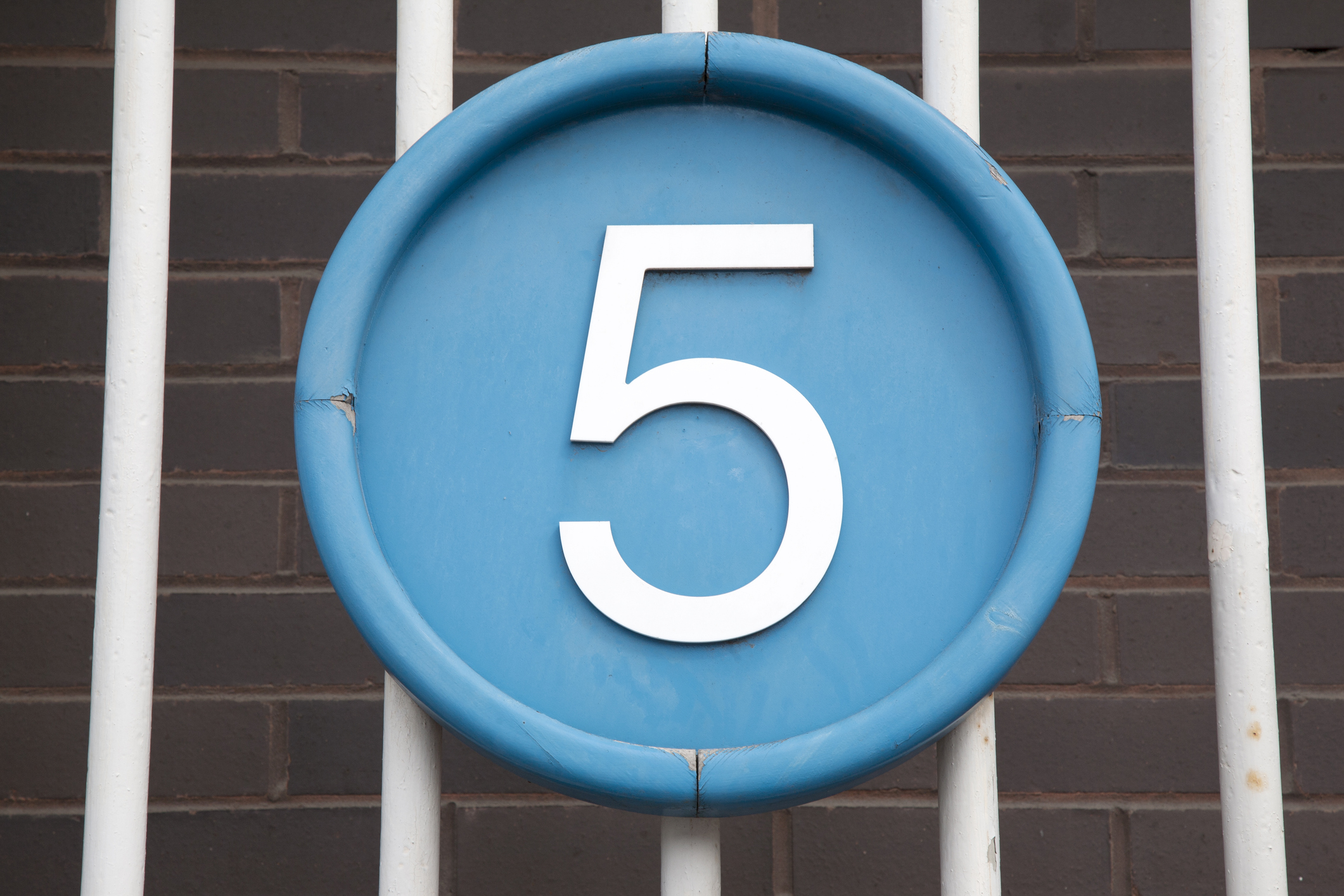 Number Five on Blue Circle against Brick Wall and Railings Background