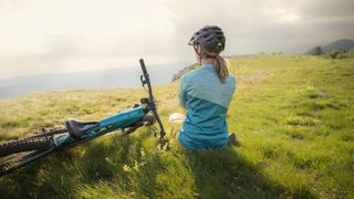 Woman sitting resting on the side of a hill with bike to one side