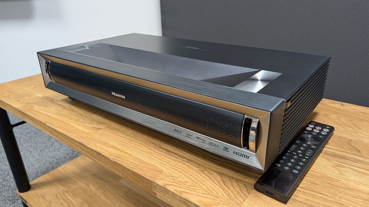 Hisense PX3-Pro ultra short throw projector on wooden AV rack next to remote