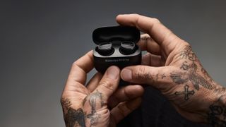 The Bowers & Wilkins Pi8 inside the charging case being held in a pair of tattooed hands