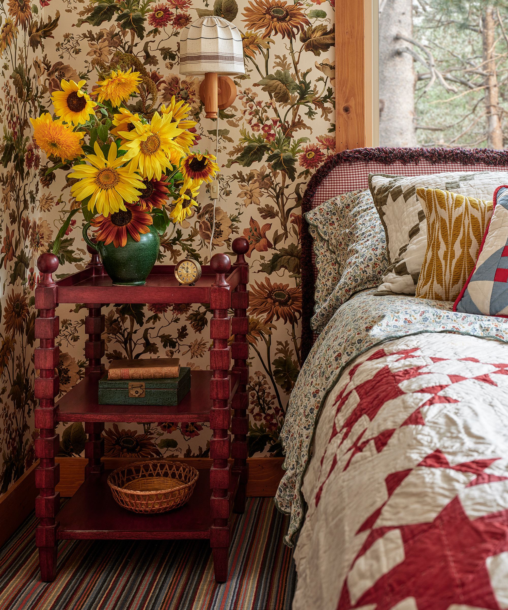 a small guest bedroom with house of hackney wallpaper, striped carpet, a red side table and a red and white bed spread quilt