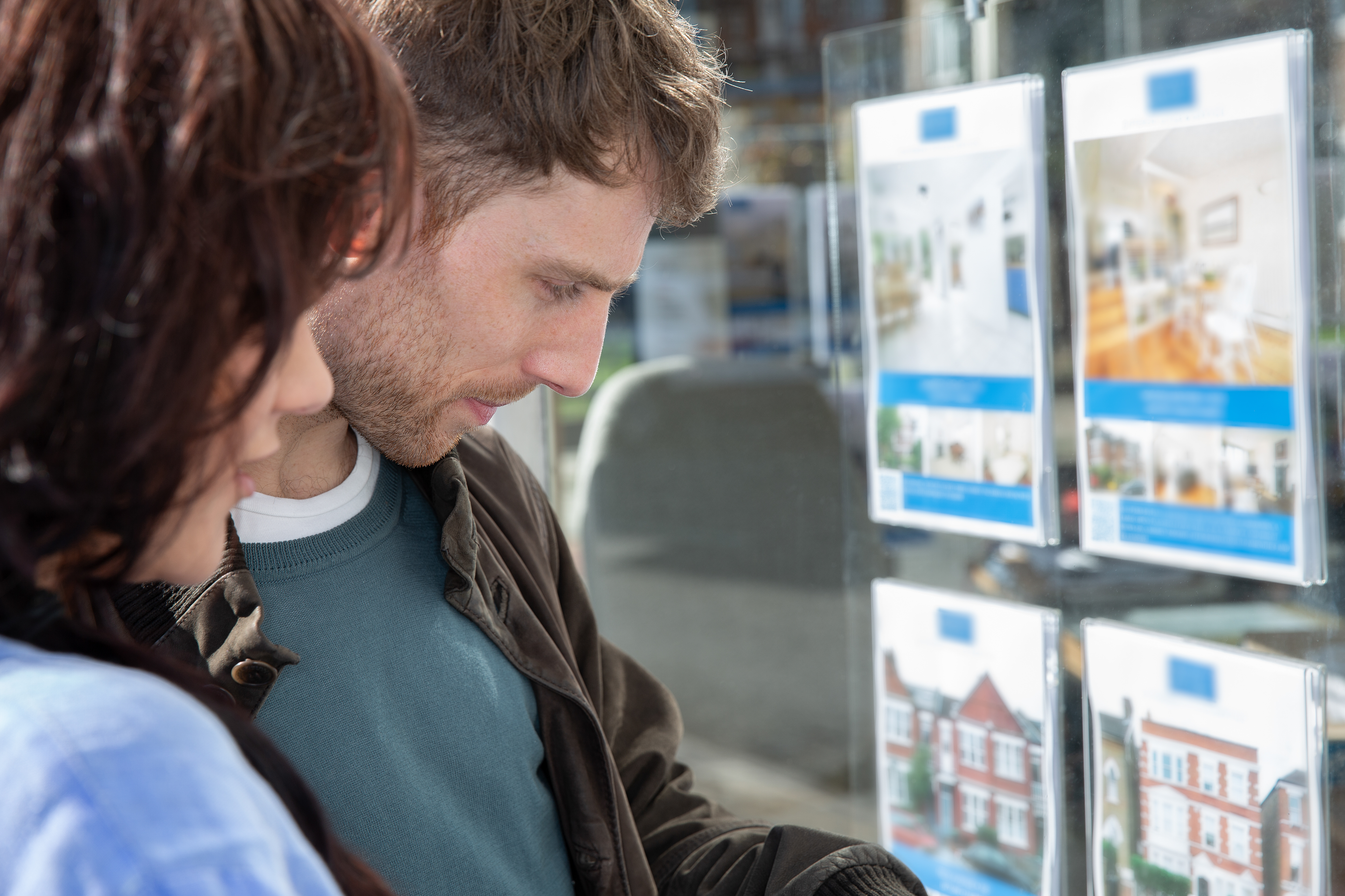 Couple look at houses for sale in estate agent window.