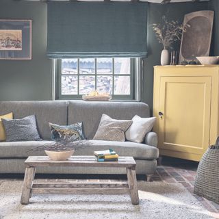snug with green walls and dark sofa paired with a yellow cabinet and grey sofa Morris & Co
