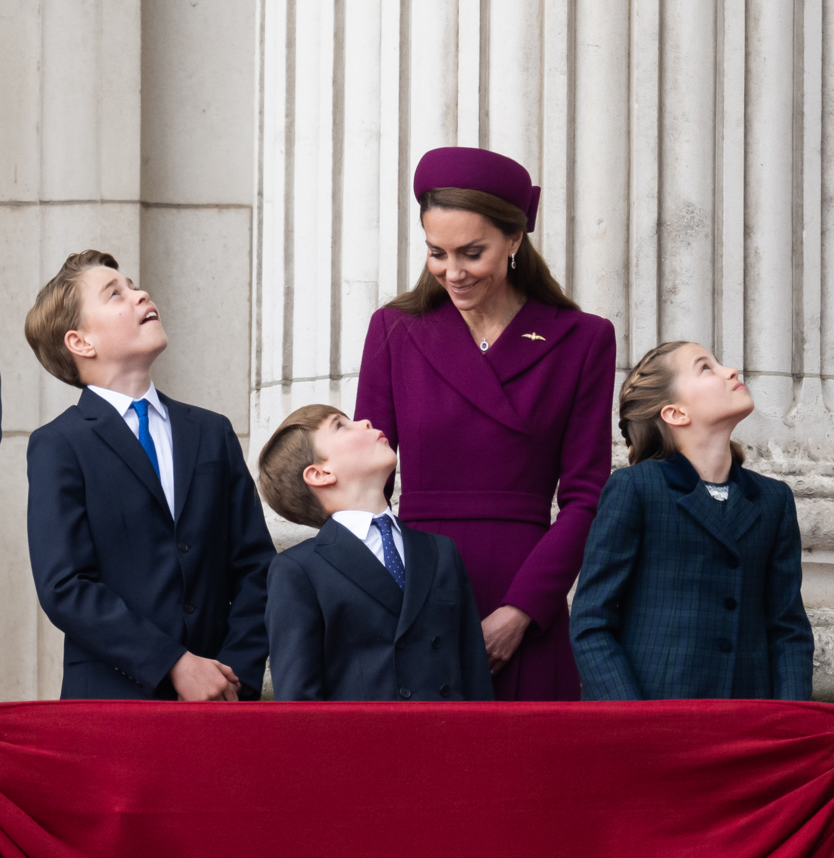 Princess Kate smiling looking at Prince George, Princess Charlotte and Prince Louis who are on the palace balcony looking up at the sky