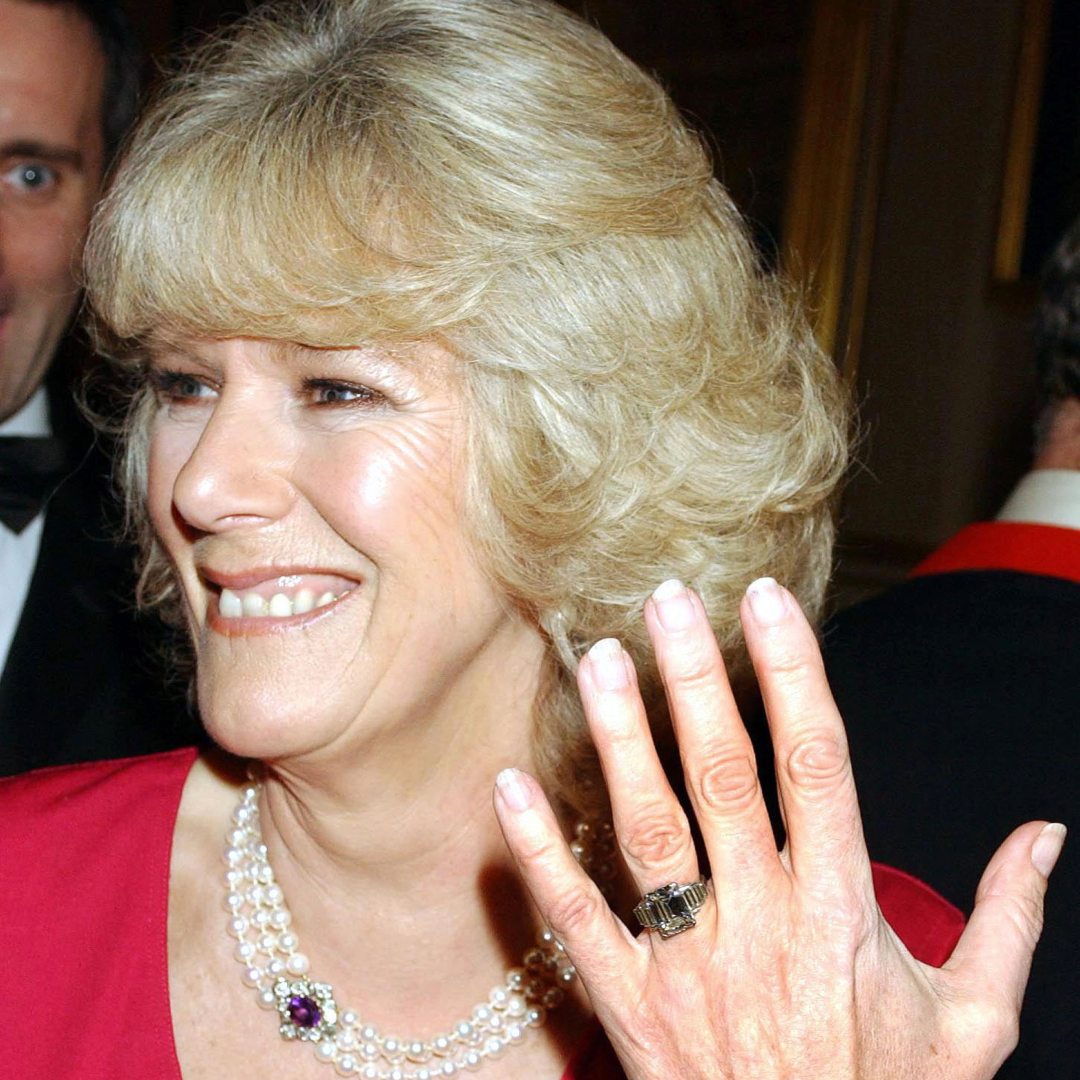 Queen Camilla in a pink coat and hat; Queen Camilla holding up her hand to show her engagement ring