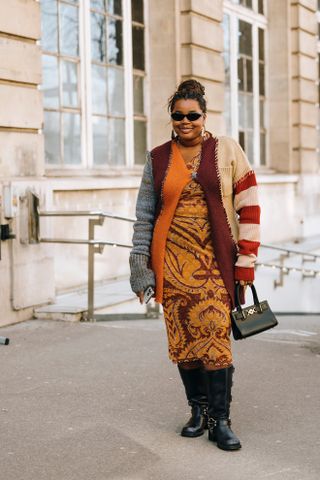 Gabriella Karefa Johnson wearing knee high black moto boots, a yellow and red dress, and colorful striped sweater