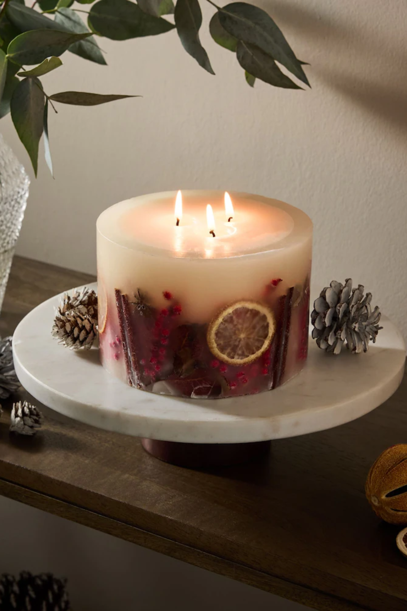 A white inclusion candle on a marble stand by some pinecones