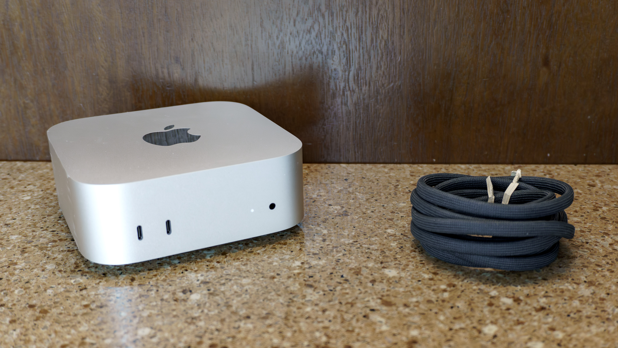 The Mac Mini with M6 unboxed on a table with its power cord next to it