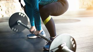 Woman demonstrates starting position of sumo deadlift with barbell