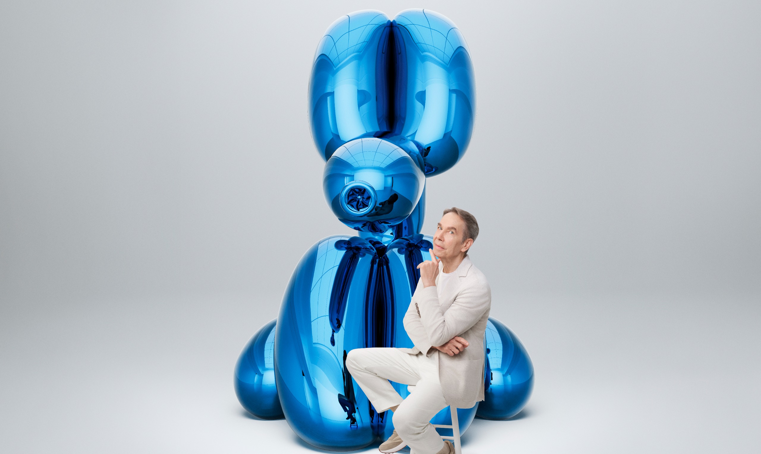 The artist sitting in front a giant blue rabbit, one of his signature sculptures