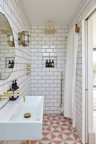 White tiled luxury bathroom, with shower, built-in niche, wall mirror, basin and brass fittings