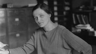 Cecilia Payne Gaposchkin sits at a desk and turns slightly toward the camera.