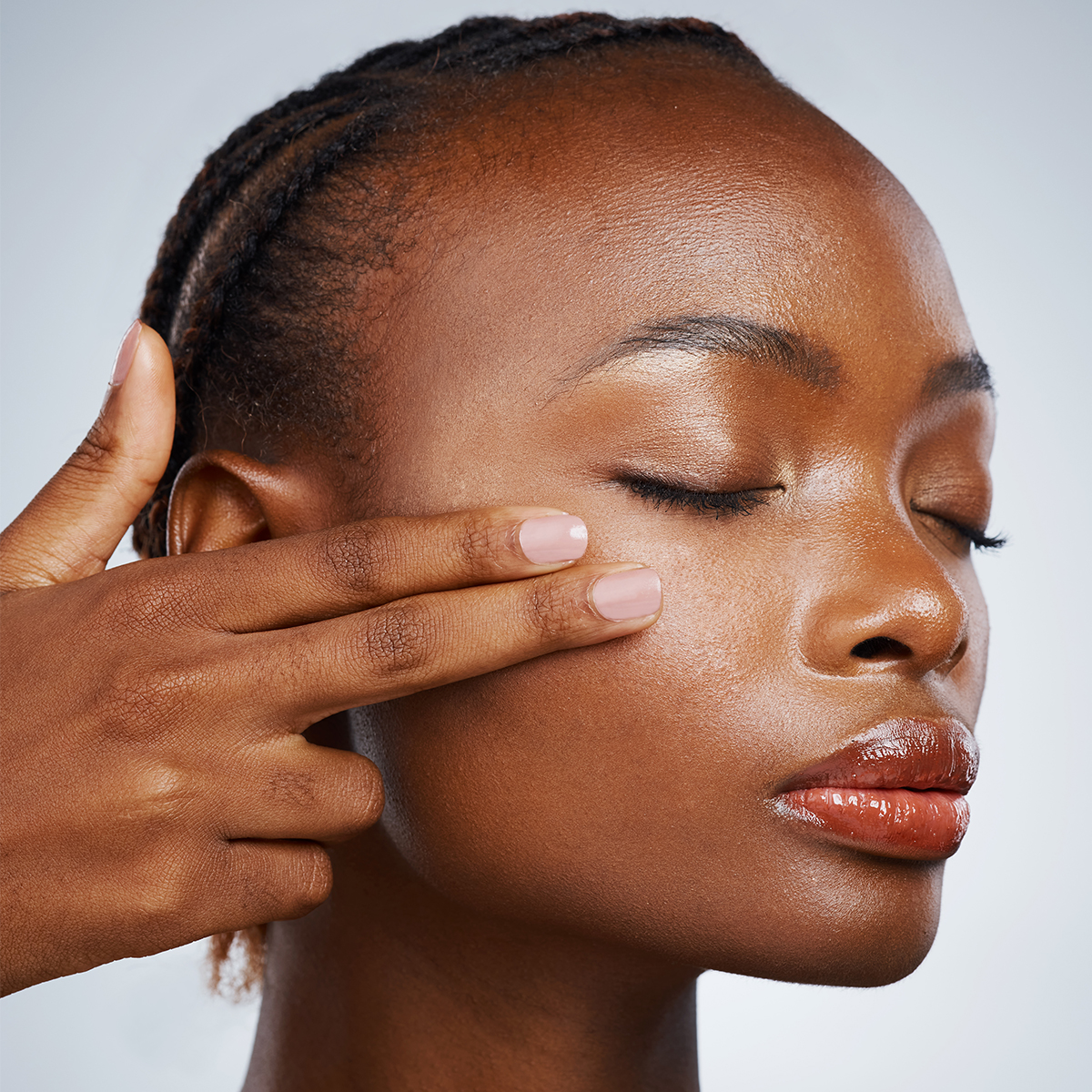 A photo of a model with her eyes closed using her fingertips to apply skincare to her cheeks