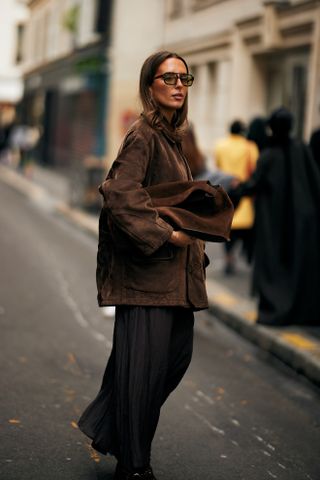 A woman at Paris Fashion Week carrying a brown suede bag and wearing a brown suede jacket and black pants