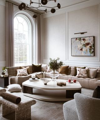 neutral living room with neutral modular sofa, large shaped coffee table, artwork and statement pendant