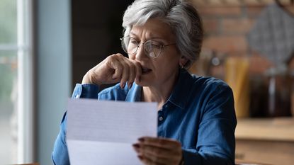 An older woman looks concerned as she looks at a letter at home.