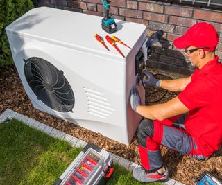 man wearing red cap and polo shirt working on heat pump unit