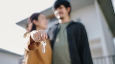 Blurry young couple standing in front of a newly purchased home holding a pair of keys