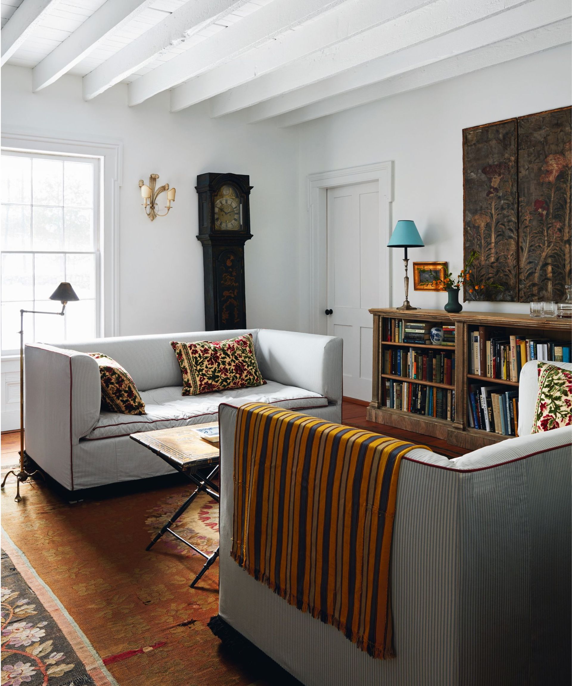 Grey sofa, black grandfather clock, wooden shelves