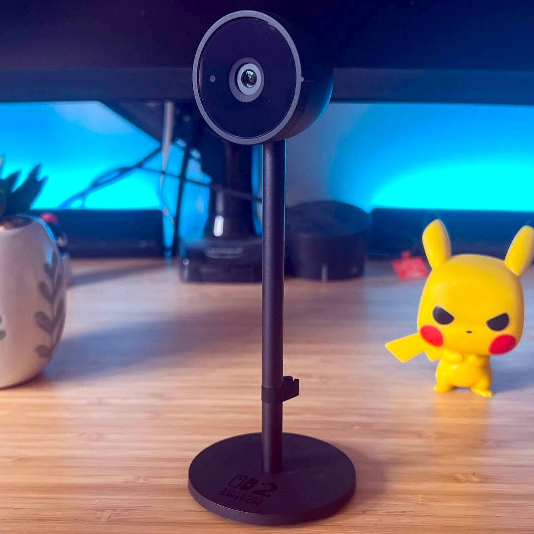 Switch 2 camera on desk with Pikachu figure on right and plant on left.