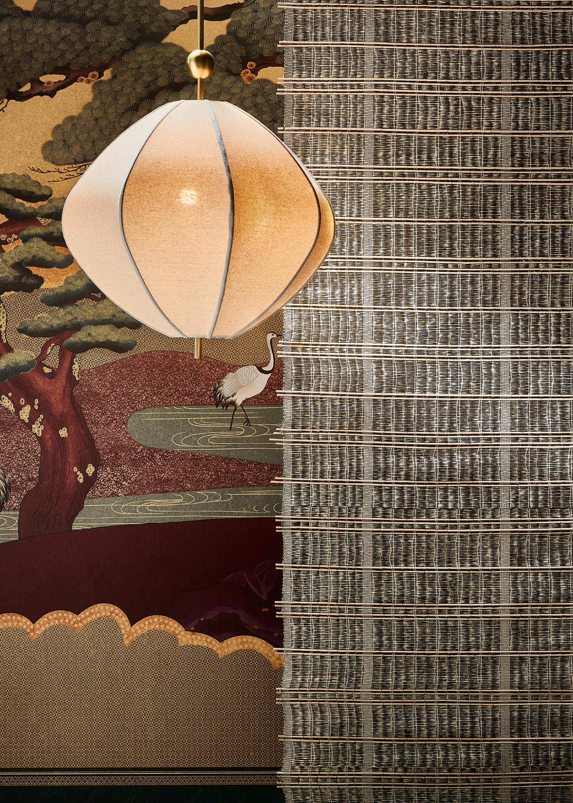 a design showcase feature a lit hanging white paper pendant against a woven screen in front of ornate wallpaper on the back wall
