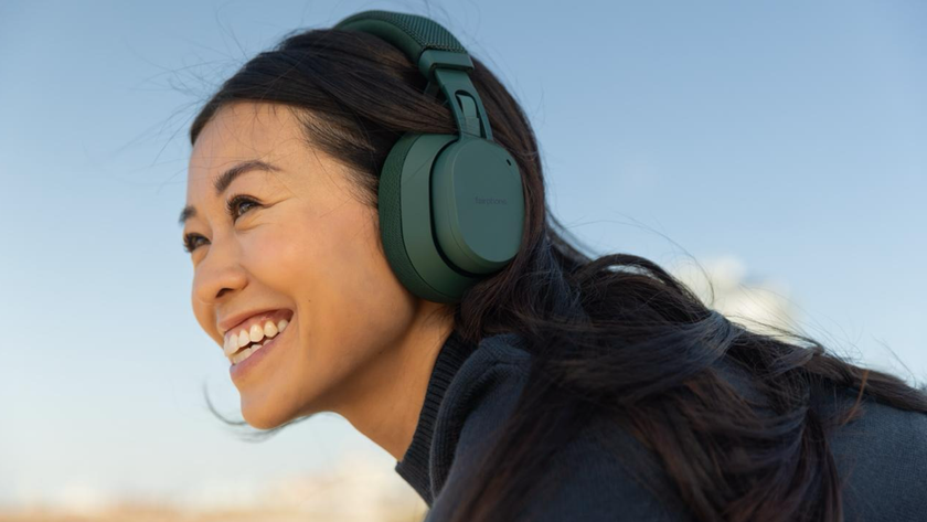 A young, smiling woman wearing a pair of fairphone fairbuds xl 2025 against a blue sky