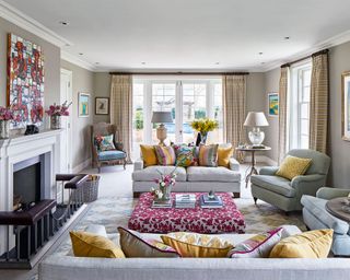 Beige living room ideas with neutral sofas and colorful yellow and pink accents in the cushions, drapes, ottoman and wall art.