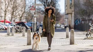 Woman walking down the street walking dog while looking at mobile phone smiling