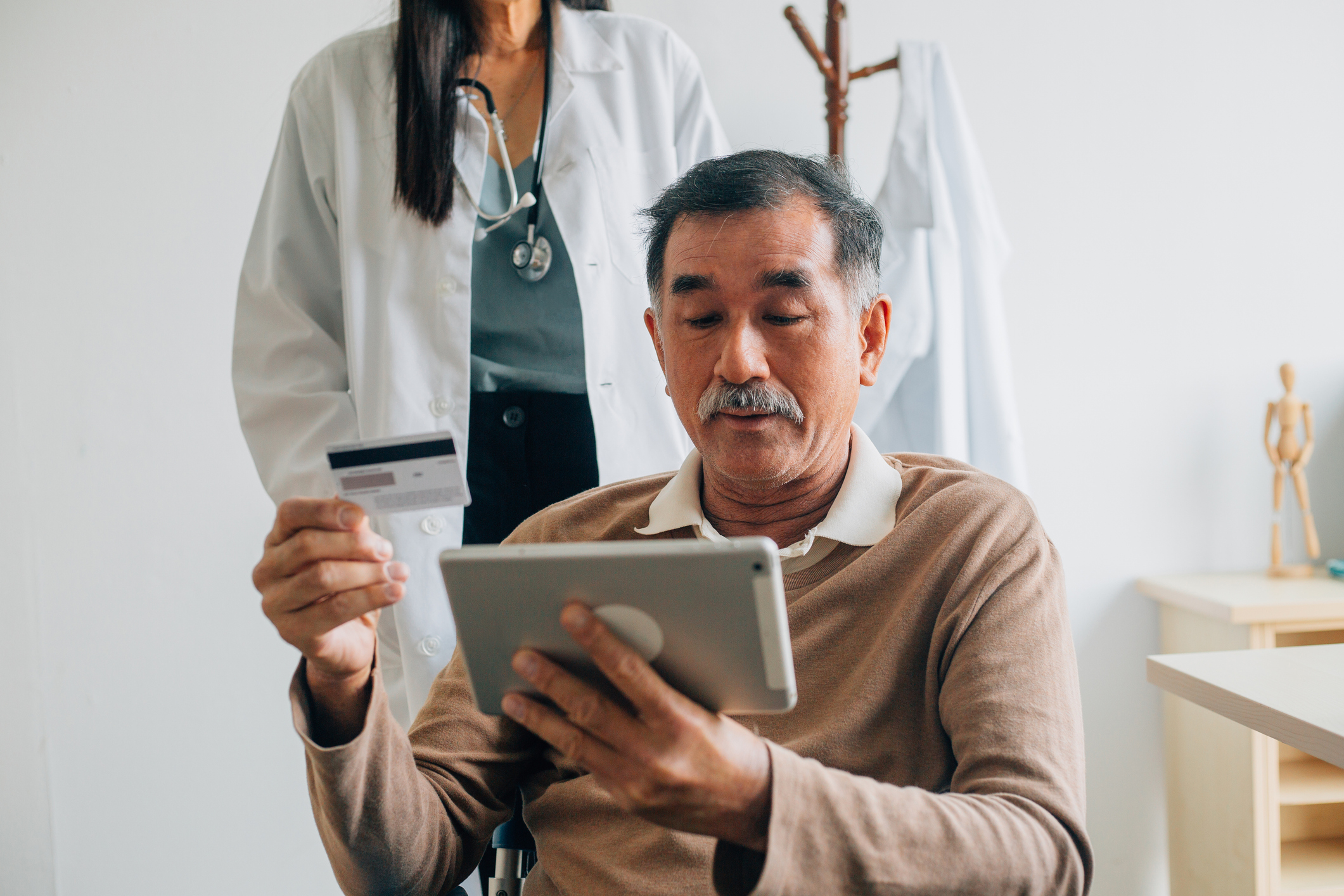 Senior patient using digital tablet and credit card making online payment while sitting on wheelchair at the hospital