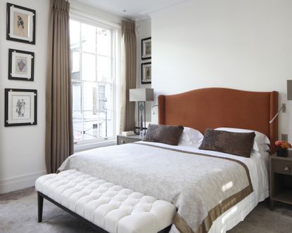 A white bedroom idea with orange headboard, taupe curtains and brown furniture