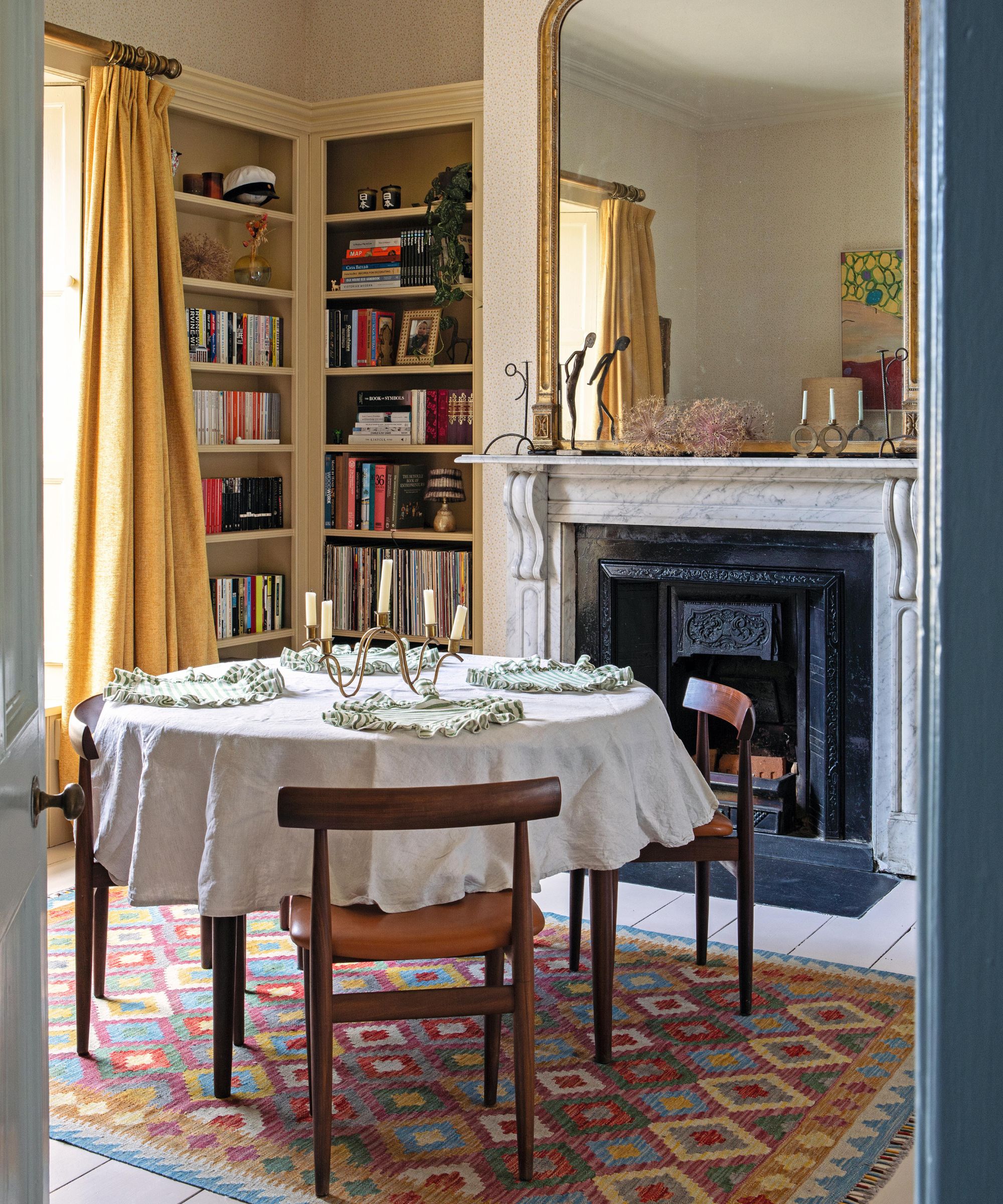 a traditional english dining room with a Victorian marble fireplace with a gold gilt mirror, round table and wooden chairs sat on a vintage rug