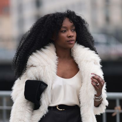 Lilian Litehiser seen wearing Beaumont white fake fur midi coat, white cotton top, Topshop grey pinstripe micro shorts, black leather / gold belt and Massimo Dutti black suede leather clutch bag, during Berlin Fashion Week AW25 on January 31, 2025 in Berlin, Germany