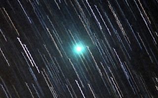 a green comet can be seen among streaks created by stars during a long exposure photograph
