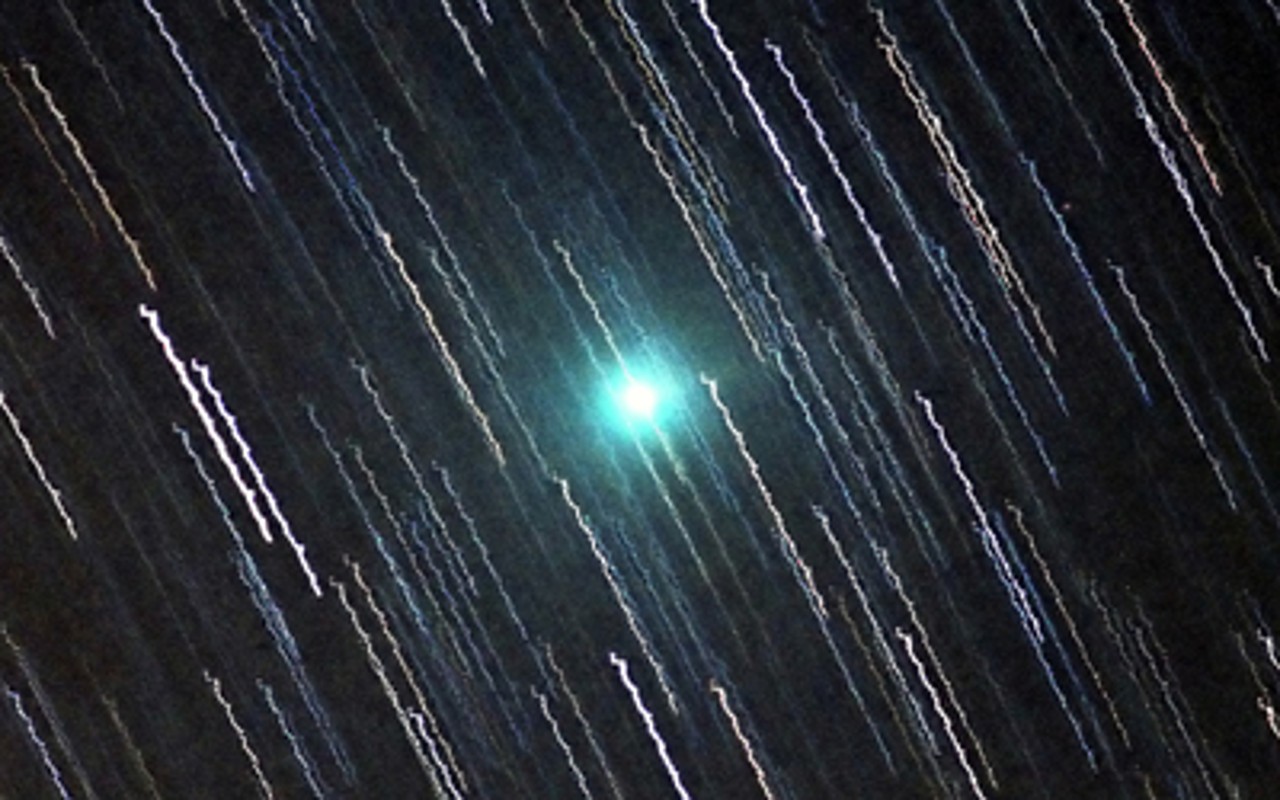 se puede ver un cometa verde entre las rayas creadas por las estrellas en una fotografía de larga exposición