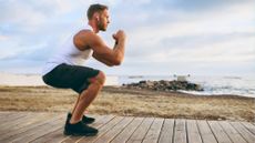 Man performing bodyweight squat outside by the ocean during outdoor workout