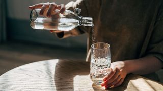 Woman's hands pouring water from glass bottle into glass