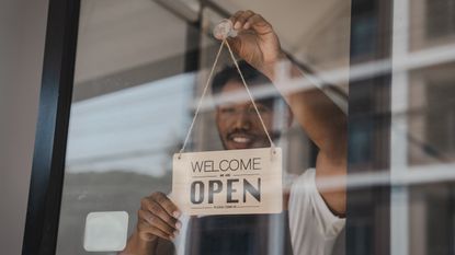 A small business owner hangs an Open sign on the door.