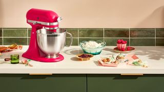 Fuscia KitchenAid stand mixer shown in green kitchen with baking equipment around it.
