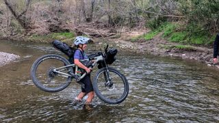 Sarah Sturm is carrying her loaded bike across a river, with water up to her knees and she's laughing