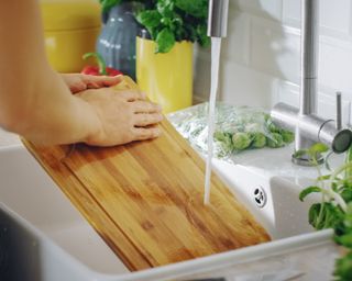 Wooden cutting board being rinsed in the sink