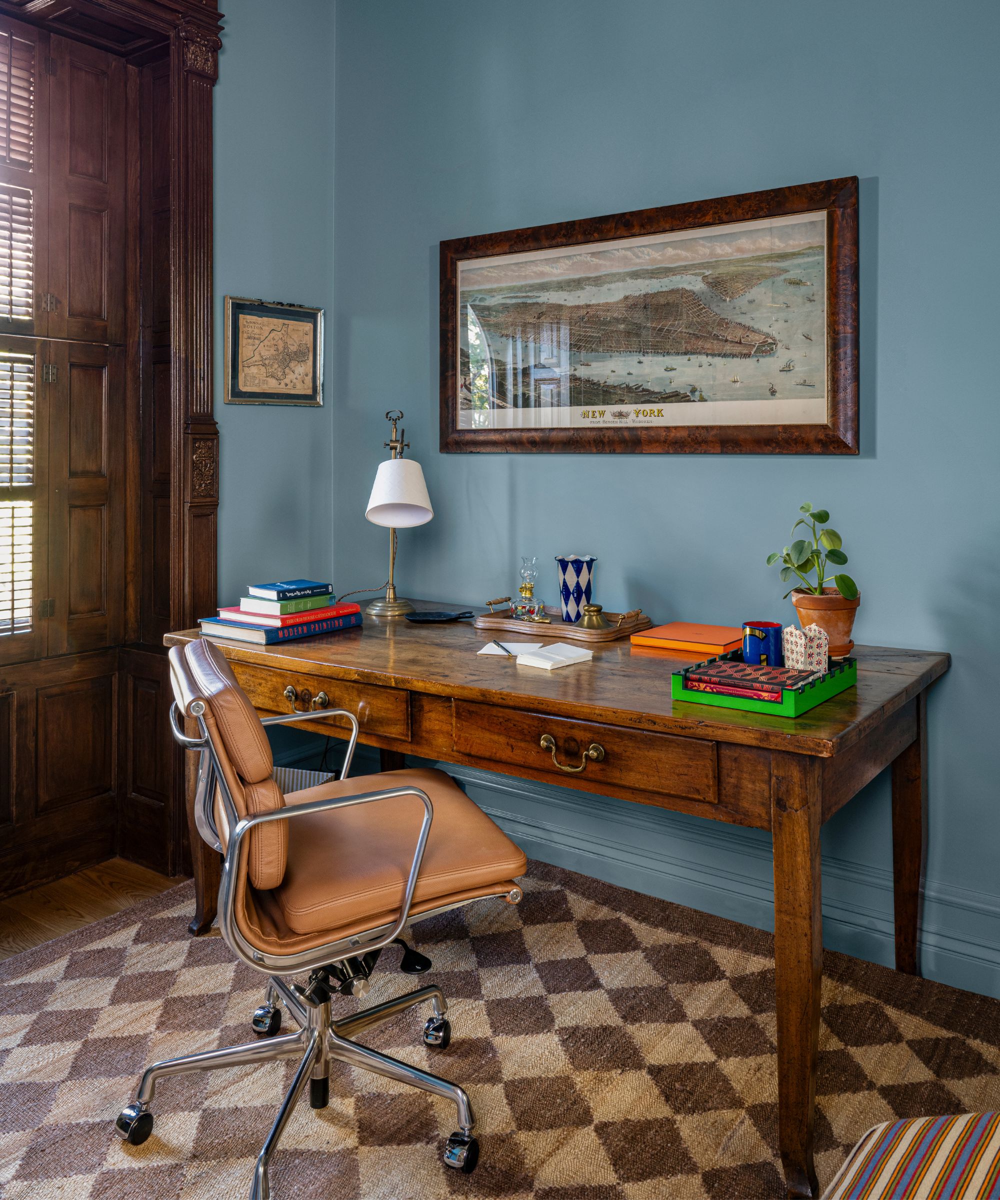 a blue home office in a new york brownstone with mahogany window and antique desk, leather chair and a woven rug