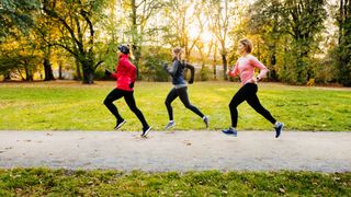 Three woman sprinting down a pathway in a park