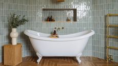 A classic white roll top bath tub in a large bathroom with blue tiled walls and a red herringbone tiled floor.
