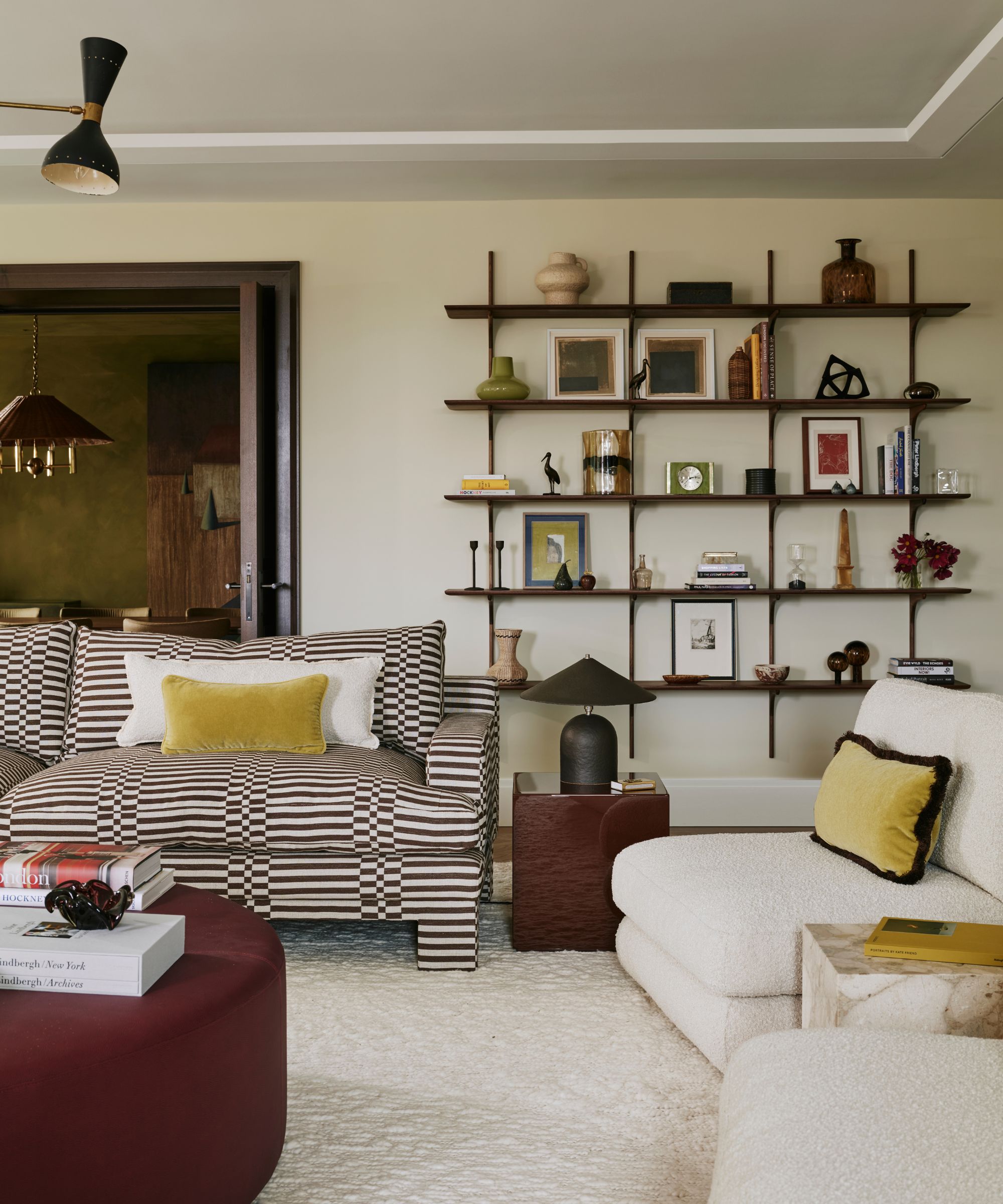 neutral cozy modern living room with sleek minimal wall shelving, a graphic printed couch, white and yellow lumbar pillows and two boucle armchairs