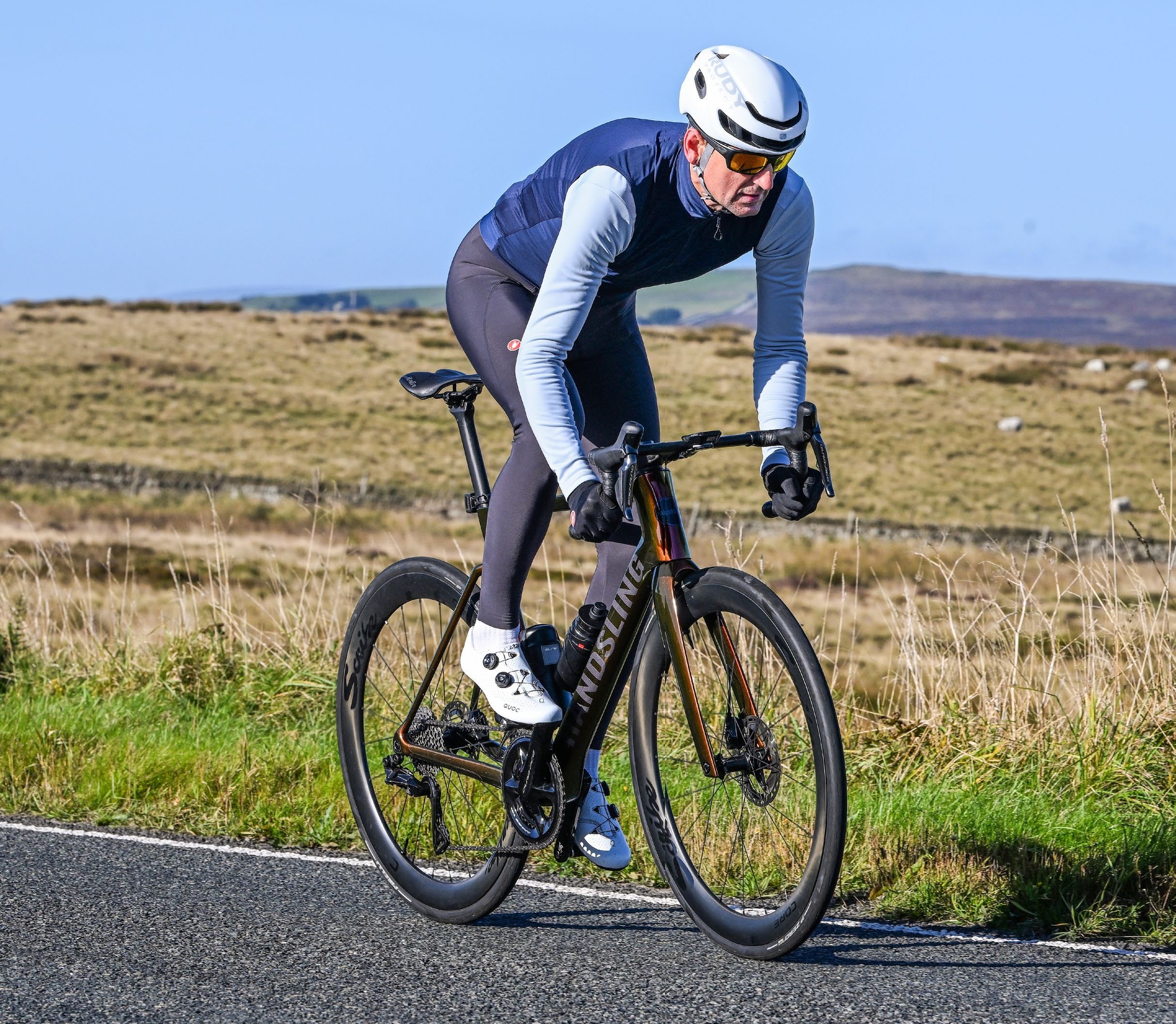 A male cyclist in winter kit riding across a road traversing open moorland
