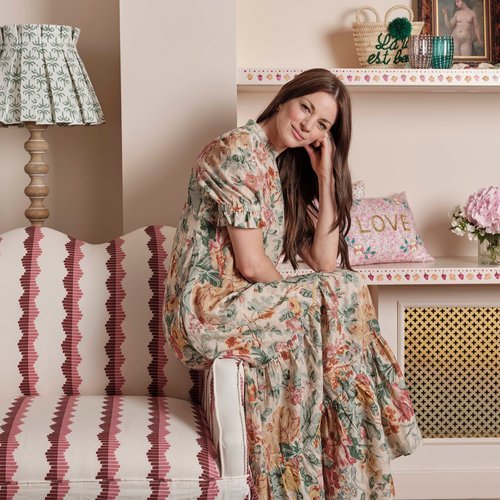 a woman in a printed dress sitting on the edge of a couch with a red and pink striped print