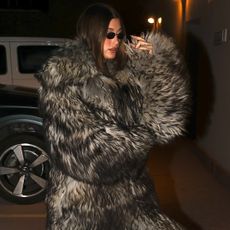 Hailey wears black sunglasses, a fur coat, and black sock boots.