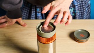 Dropping the coffee filter into he Wacaco Pipamoka portable coffee maker in front of a blue background.