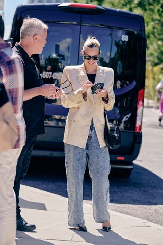 woman on her phone at new york fashion week wearing a tan blazer and blue jeans